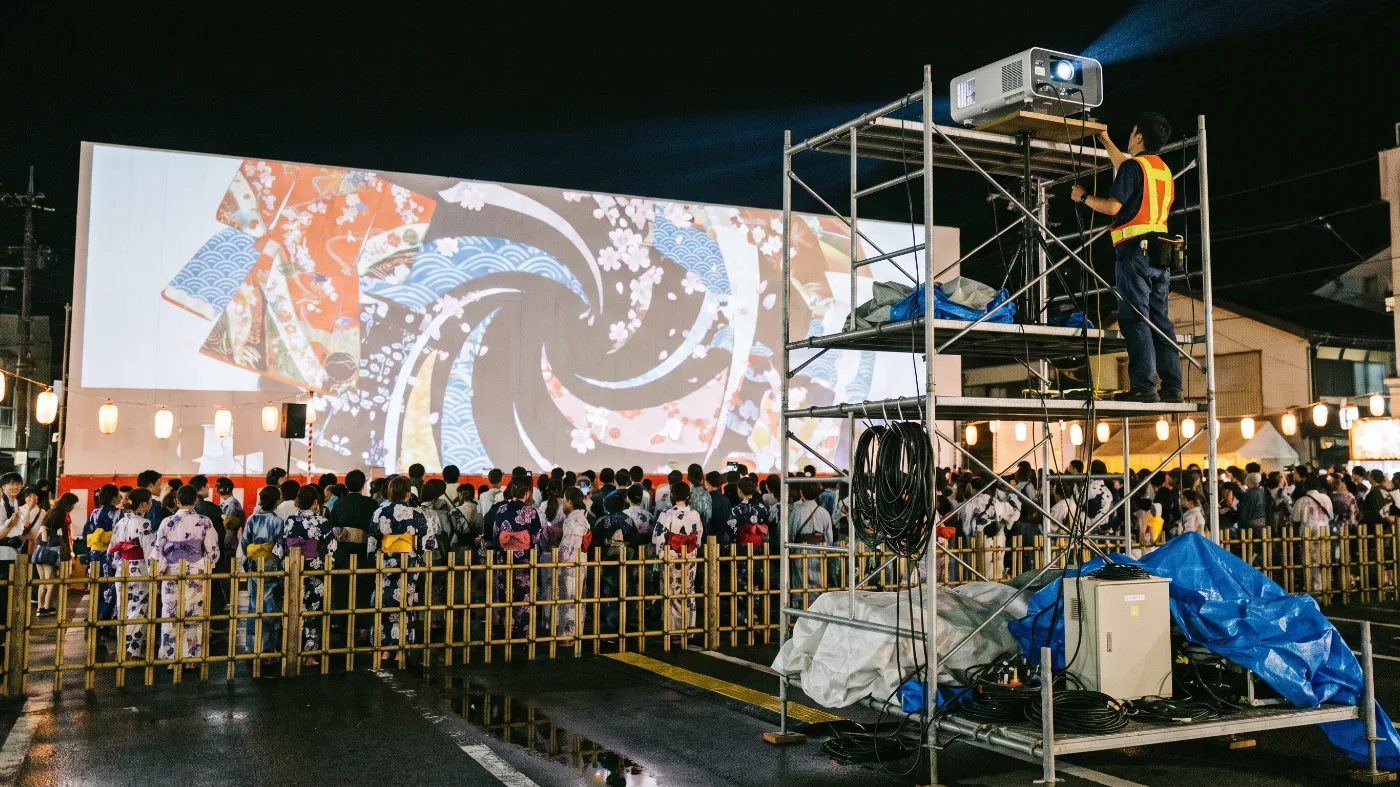 祭り会場での仮設ステージへの投影と、足場に設置した高輝度プロジェクター（イメージ）